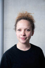 Corinne Meredith. A headshot of a smiling person with tied back light brown tightly curled hair