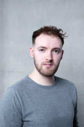 Ted Wilkinson. A headshot of a person wearing a grey tshirt and short brown hair and stubble